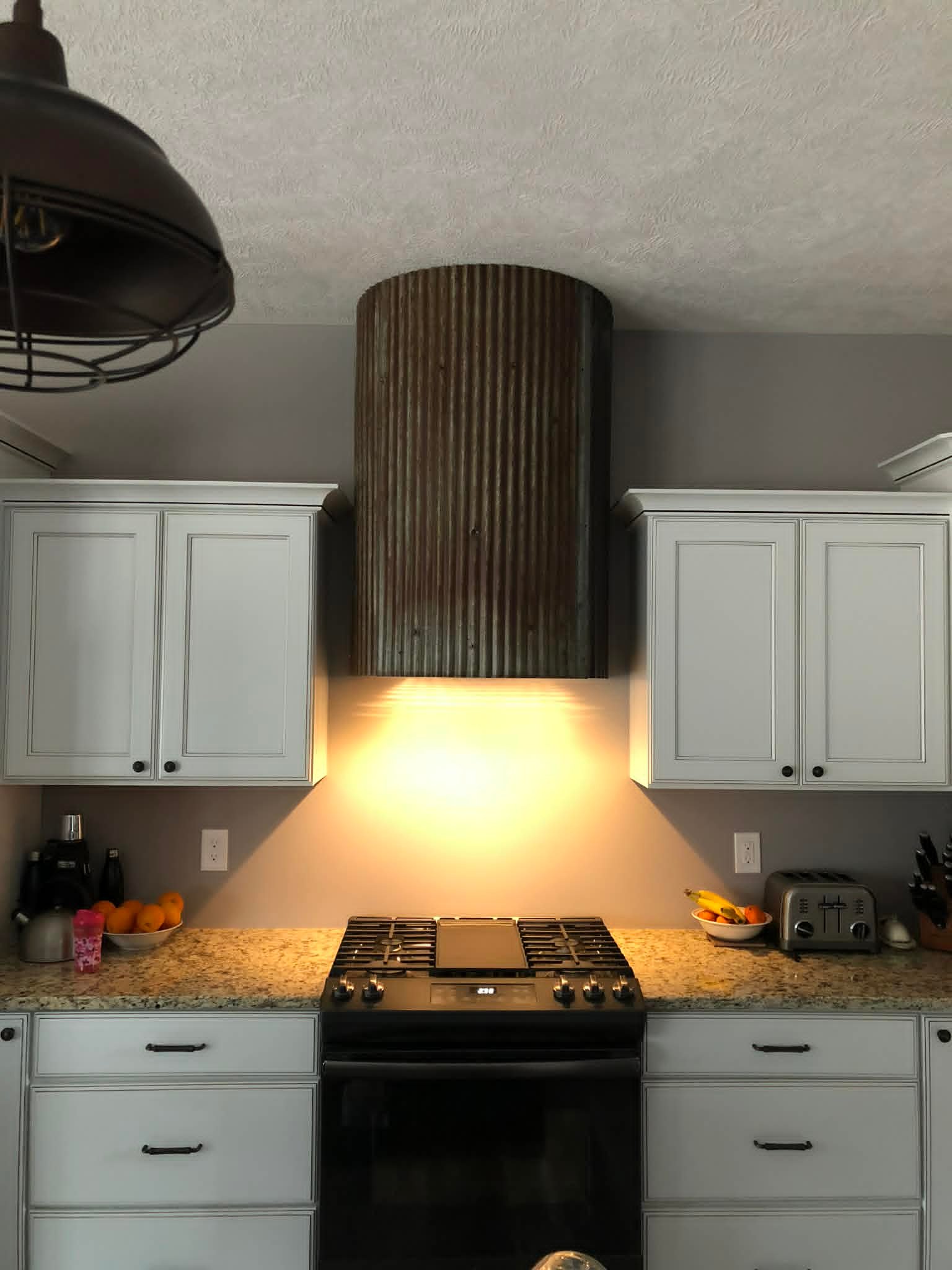 Finished kitchen range hood with corrugated metal surround and warm task lighting